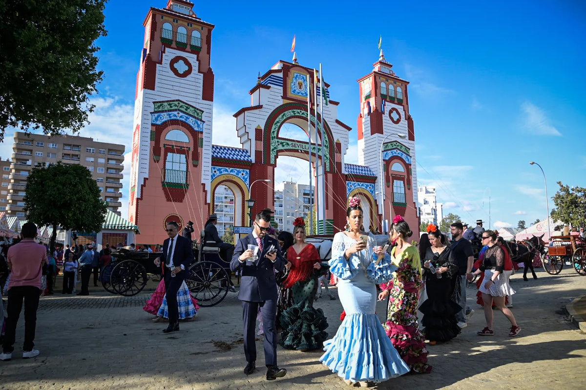 Feriantes vestidos de flamenca llegando a la portada de la Feria de Sevilla